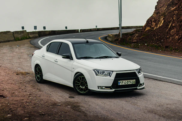A sleek white sedan parked on a winding mountain road with lush greenery around.
