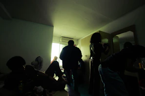 A dimly lit room with eerie red lighting and shadowy figures preparing for a jubensha session