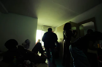 A dimly lit room with eerie red lighting and shadowy figures preparing for a jubensha session