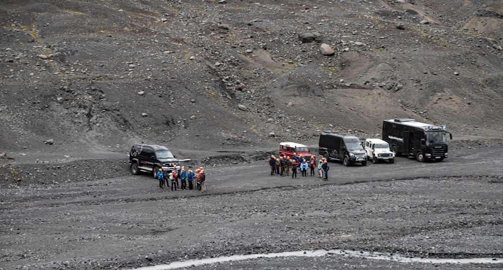 a group of people standing next to trucks on a dirt road