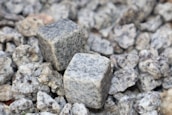 Two square-shaped granite cubes are placed on a bed of smaller irregularly shaped granite rocks, with a variety of textures and shades of gray visible.