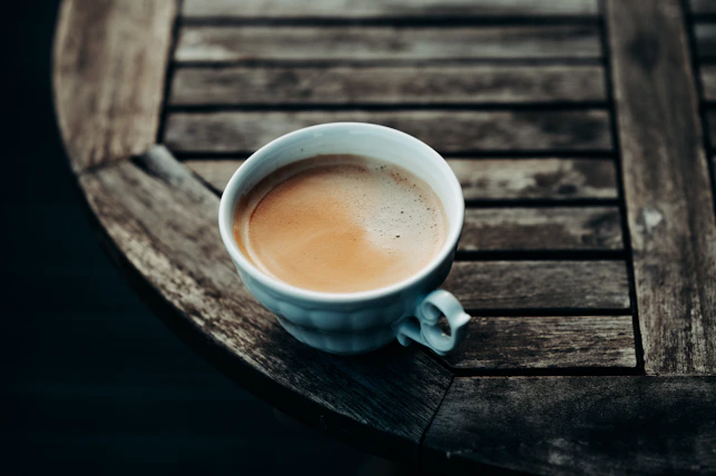 A steaming cup of coffee placed on a rustic wooden table.