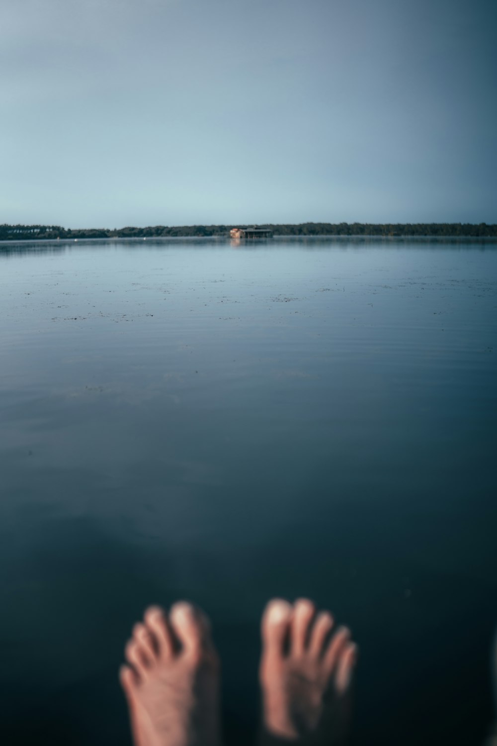 a person's feet in the water with a house in the distance