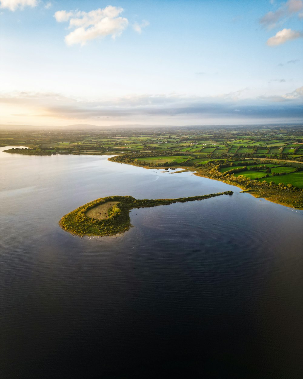 a large body of water surrounded by lush green fields