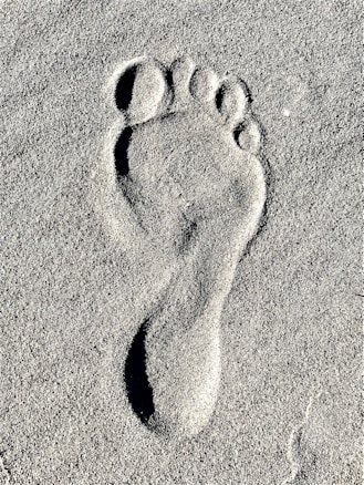 A single footprint is imprinted in soft sand, capturing the detailed contours of the toes and heel.