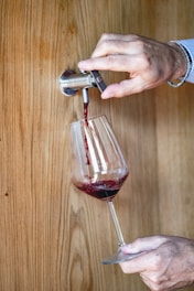 Close-up of a hand pouring red Syriac wine into a glass.