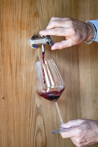 Close-up of a hand pouring red wine into a glass.