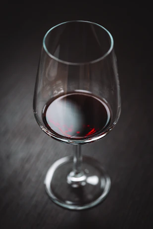 A glass of deep red wine on a polished black surface, reflecting subtle champagne accents.