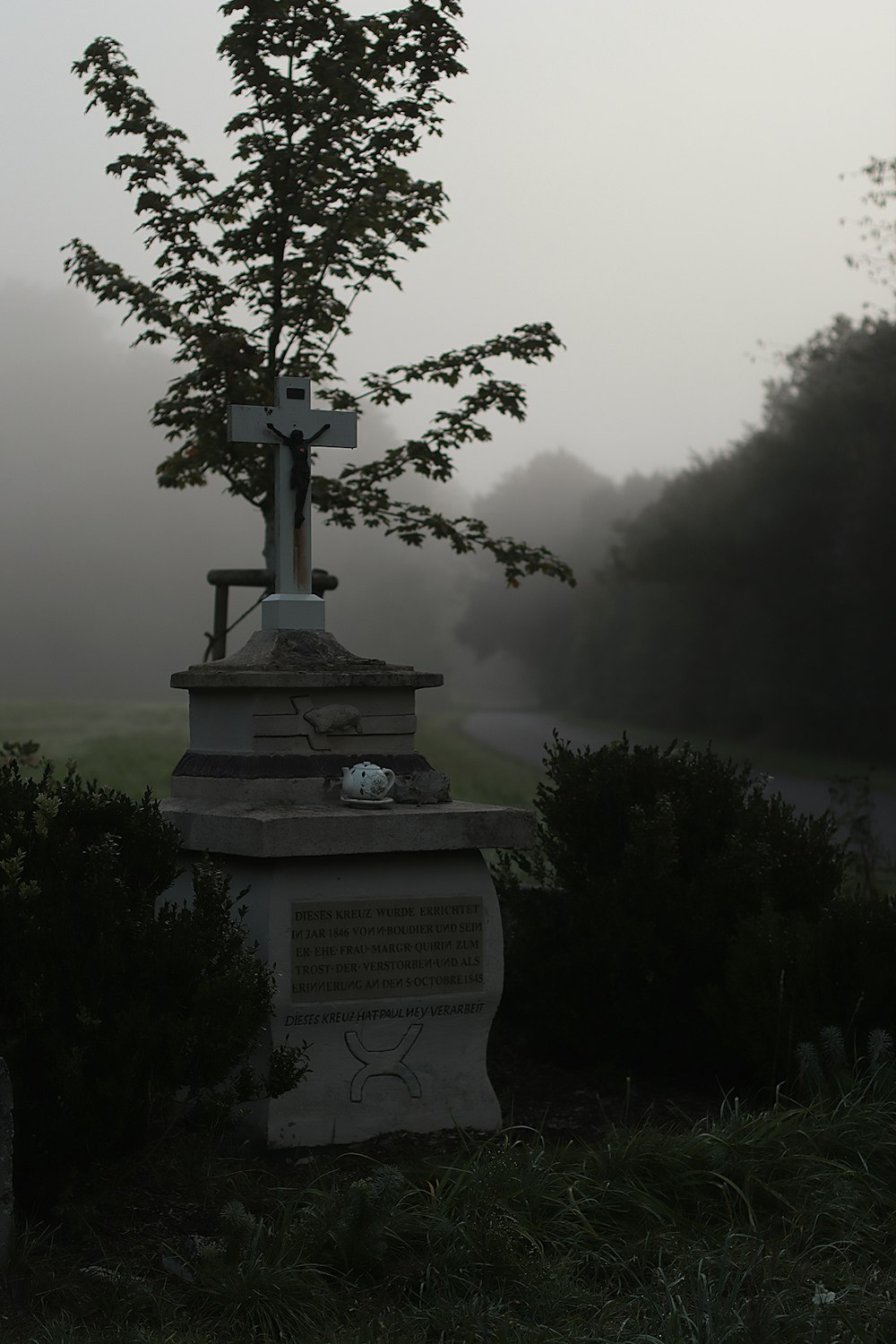 a cemetery with a cross and a tree in the fog