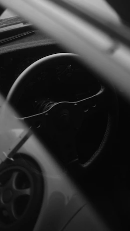 Black and white artistic photo of a car's steering wheel and dashboard.