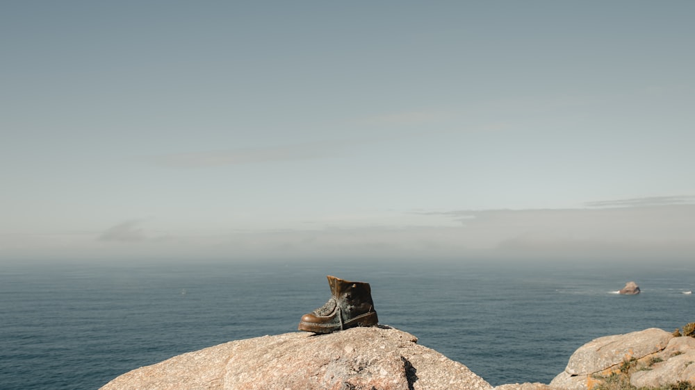a pair of boots sitting on top of a rock near the ocean