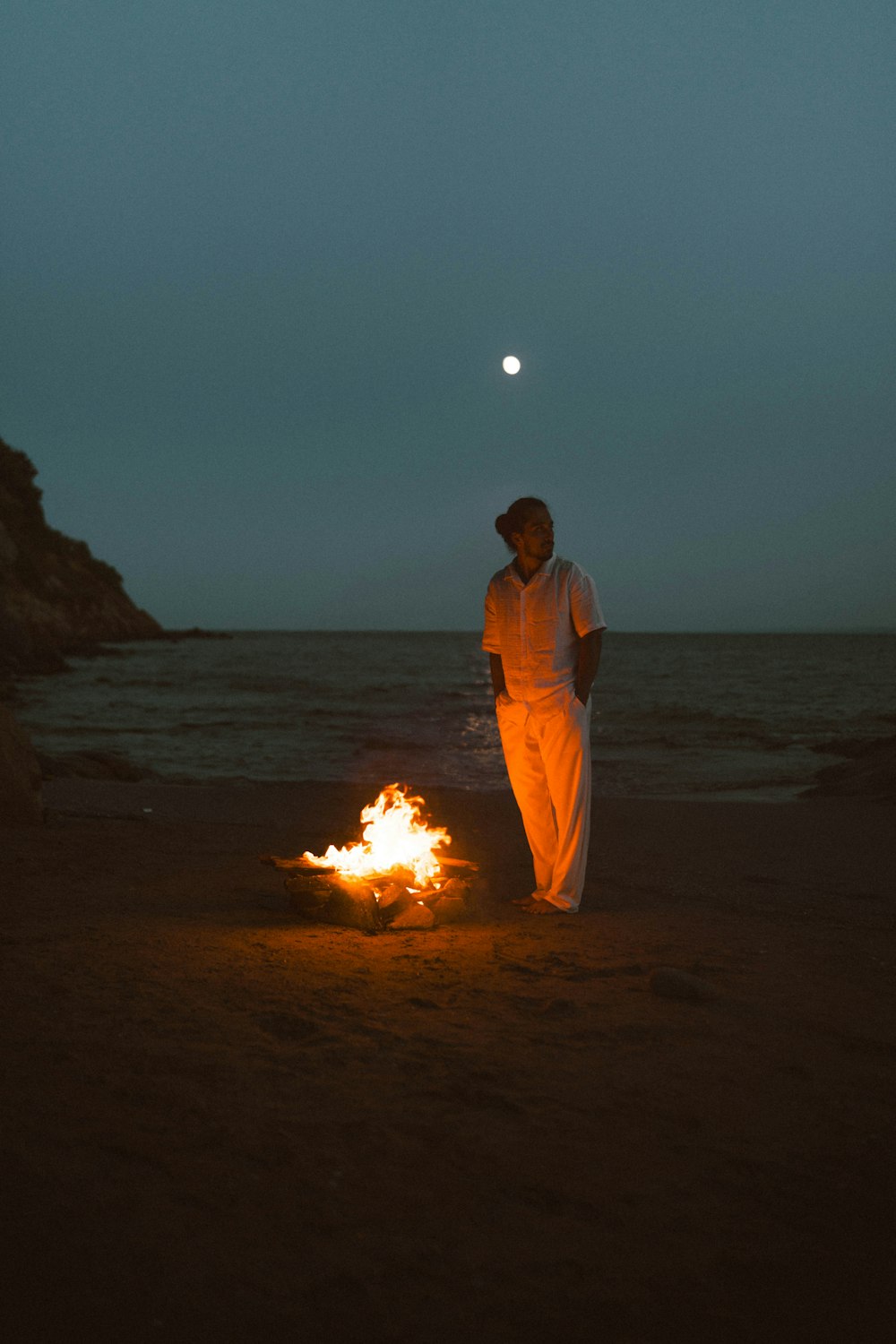 a man standing next to a fire on a beach