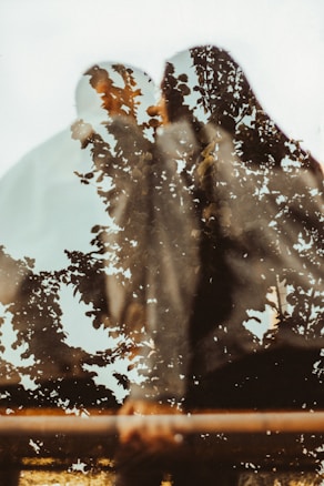 A symbolic double exposure photograph features silhouettes of people intertwined with the image of lush, leafy tree branches. The merging creates a dreamy and artistic effect, blending human forms with nature.