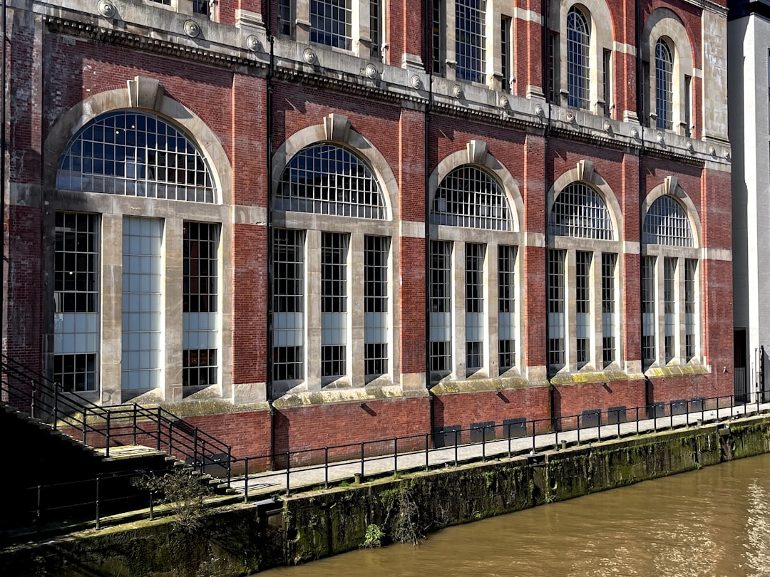 a brick building with arched windows next to a body of water, Brick façade with massive windows in Bristol