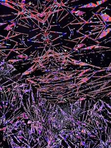 An abstract digital artwork featuring a multitude of intersecting geometric shapes and lines in vivid colors against a dark background. The overlapping forms create a sense of depth and motion, with vibrant shades of red, blue, pink, and purple standing out prominently.