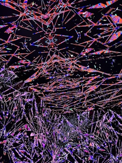 An abstract digital artwork featuring a multitude of intersecting geometric shapes and lines in vivid colors against a dark background. The overlapping forms create a sense of depth and motion, with vibrant shades of red, blue, pink, and purple standing out prominently.