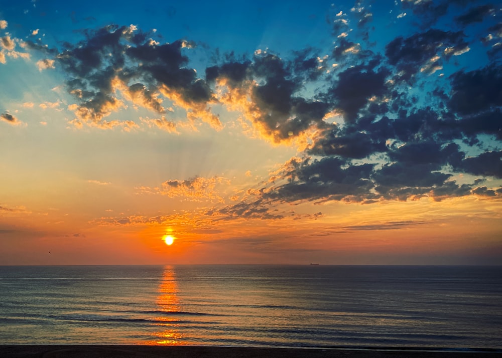 the sun is setting over the ocean on a cloudy day