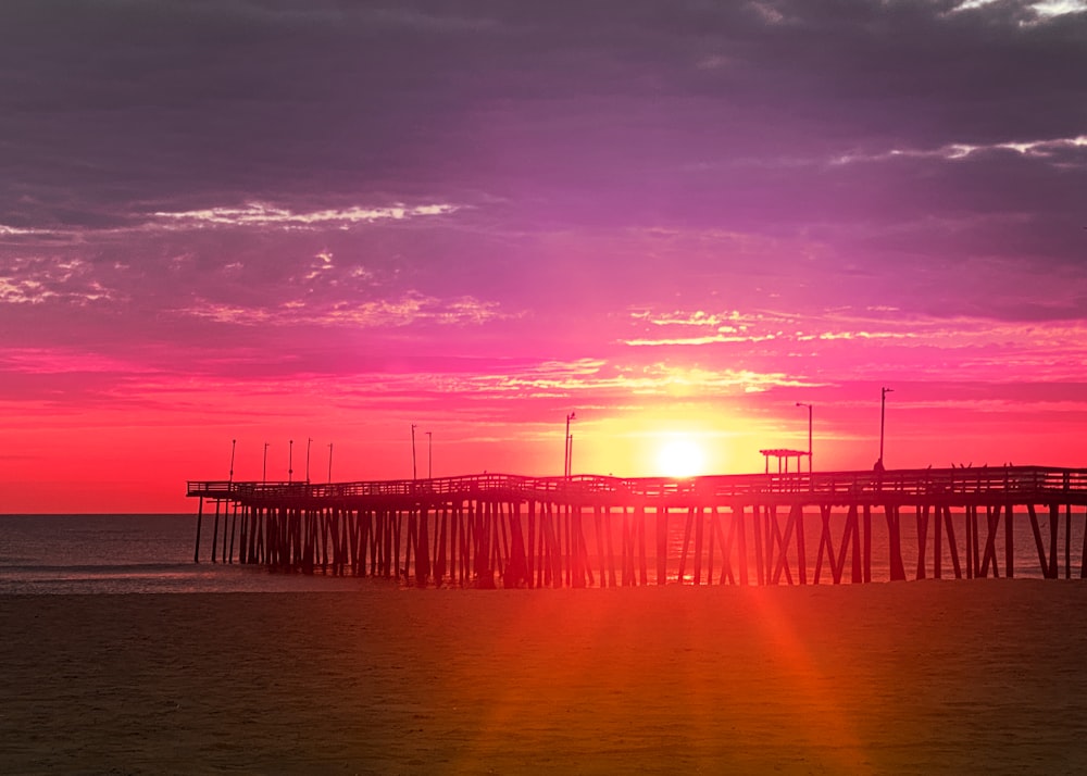 the sun is setting over a pier on the beach
