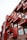 A multi-story building with a modern design featuring red protruding balconies, each adorned with potted plants. The structure includes large windows and a combination of red and rustic brown materials, creating a striking architectural aesthetic.
