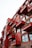 A multi-story building with a modern design featuring red protruding balconies, each adorned with potted plants. The structure includes large windows and a combination of red and rustic brown materials, creating a striking architectural aesthetic.