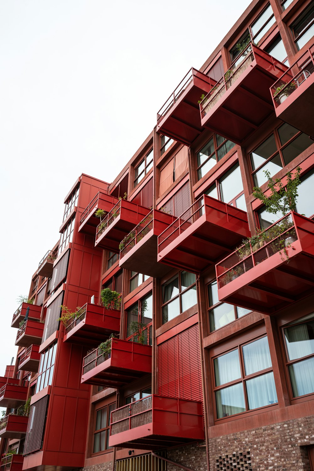 a tall red building with balconies and plants on the balconies