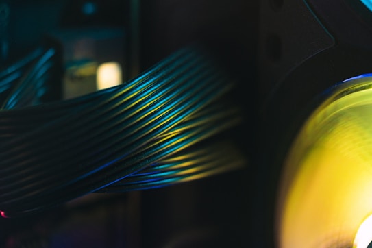 A close-up view of computer cables with a glowing green and yellow light on the right side. The cables are bundled together, creating a sense of order and structure. The lighting casts a soft gradient of colors across the cables, creating a visually appealing pattern.