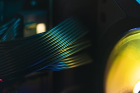 A close-up view of computer cables with a glowing green and yellow light on the right side. The cables are bundled together, creating a sense of order and structure. The lighting casts a soft gradient of colors across the cables, creating a visually appealing pattern.