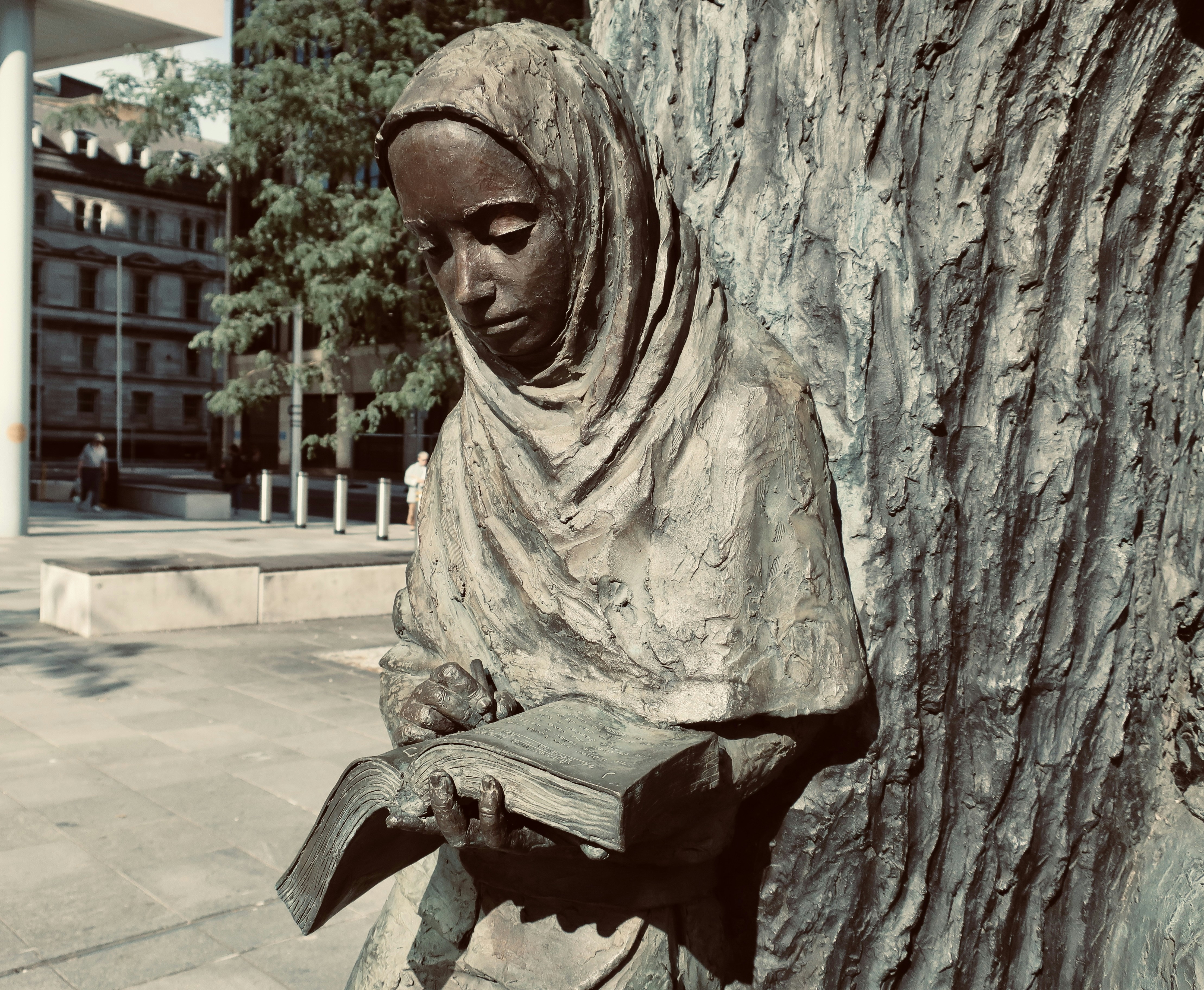 a statue of a woman reading a book next to a tree