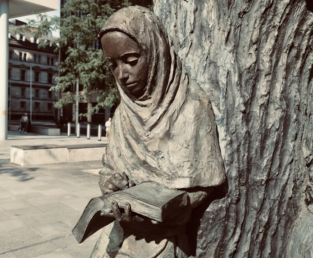 a statue of a woman reading a book next to a tree
