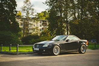 A black Mercedes convertible parked in front of a modern Bavarian building with clean lines.