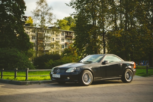 A black Mercedes convertible parked in front of a modern Bavarian building with clean lines.