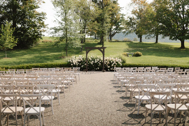 Sunlit garden ceremony setup with elegant floral arches and white chairs.