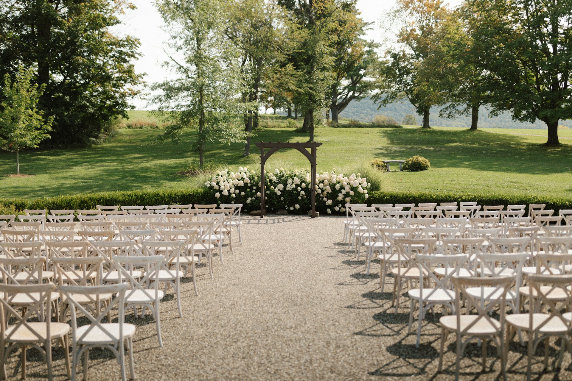 A serene outdoor wedding ceremony set against a picturesque landscape, featuring an elegant arch adorned with white flowers.