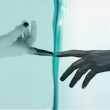 Two hands are depicted reaching towards each other with only their fingertips touching, separated by a transparent barrier. The left hand appears to be in a black and white style, while the right hand has a darker tone against a pale turquoise background.