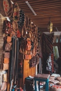 A market stall showcasing a variety of handmade leather goods, including bags and belts, hanging neatly on display. Intricately woven textiles and rugs are draped in the background, adding vibrant patterns to the scene. A rustic wooden table and several traditional items create a warm, inviting ambiance.