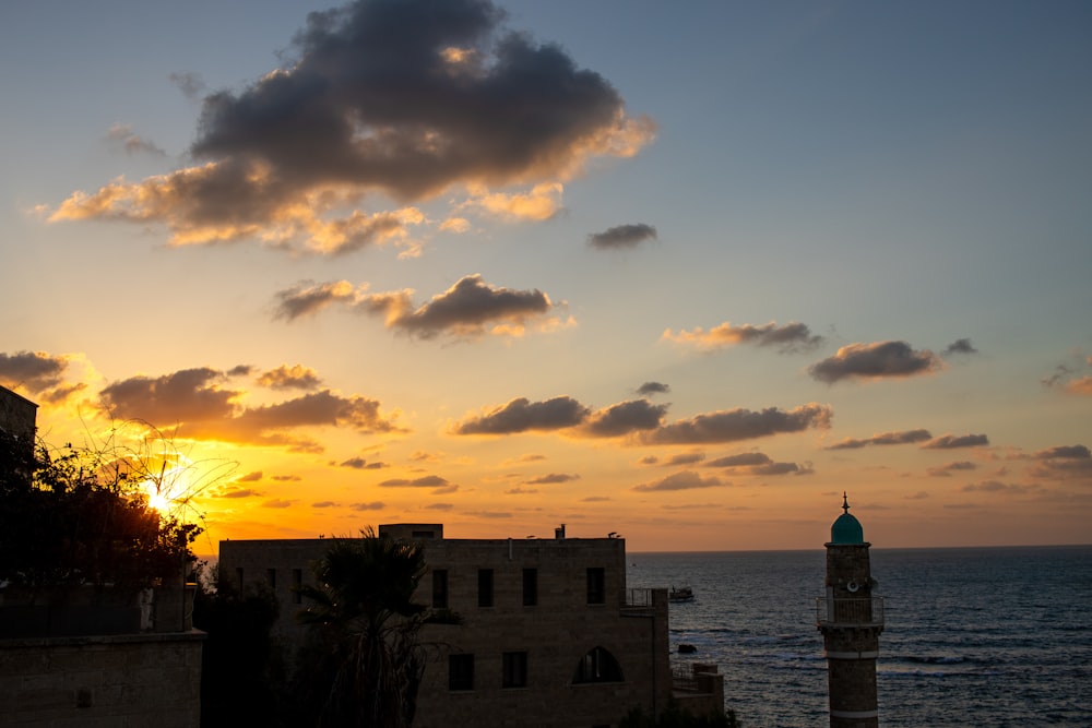 the sun is setting over the ocean with a tower in the foreground