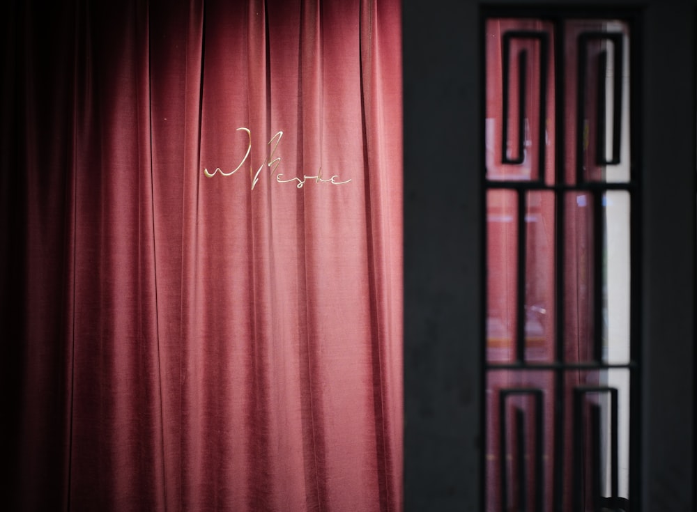 a red curtain with writing on it next to a window