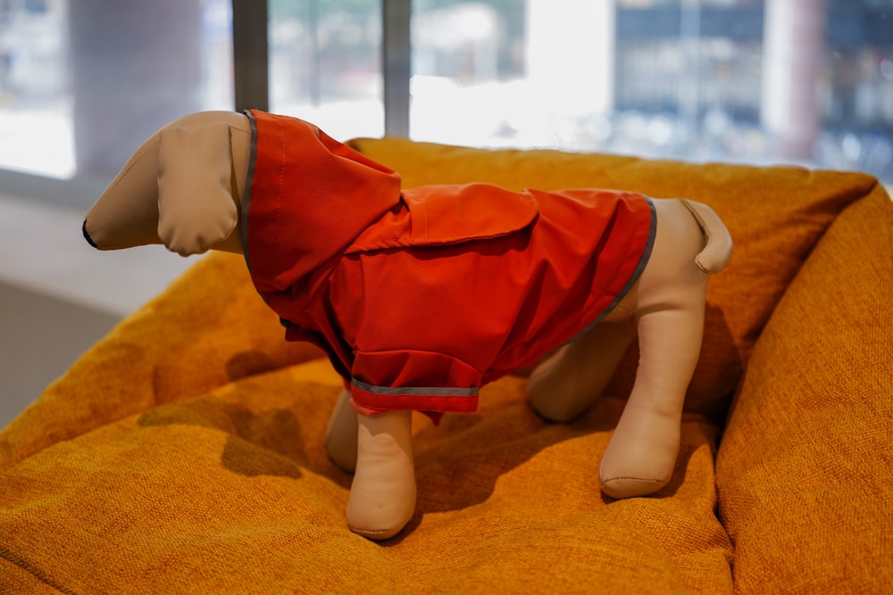 a stuffed dog wearing a red jacket on a couch