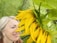 A close-up of a smiling woman holding a hemp leaf in a sunlit field.