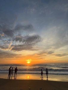 A group of tourists watching a colorful sunset over the Pacific Ocean from a beach.