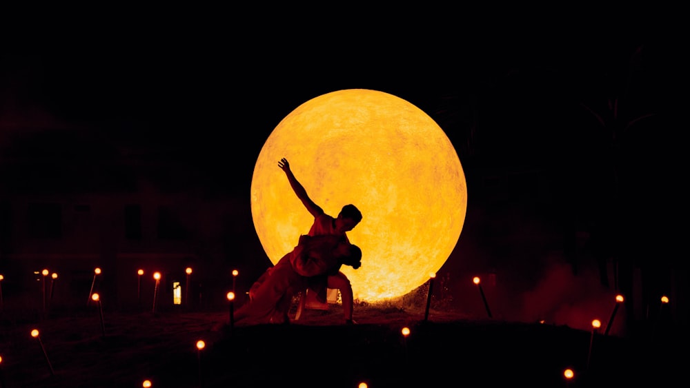 um homem parado em frente a uma lua amarela gigante