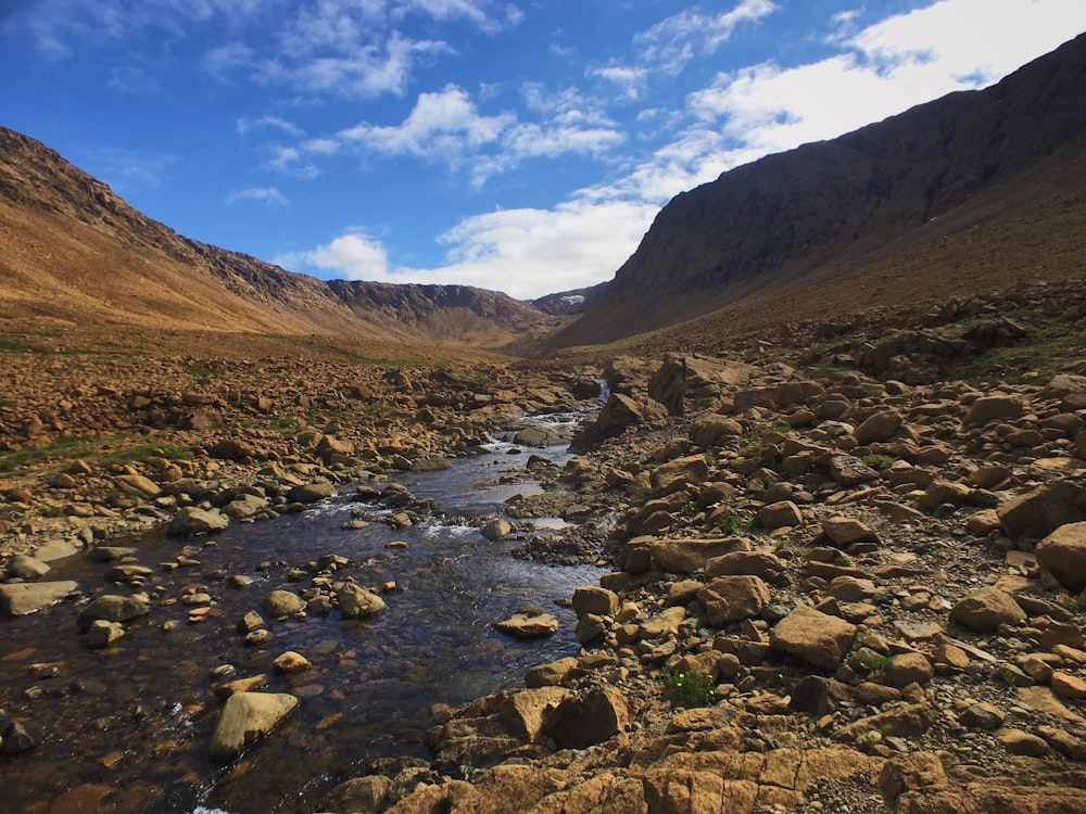 a rocky river running through a valley surrounded by mountains