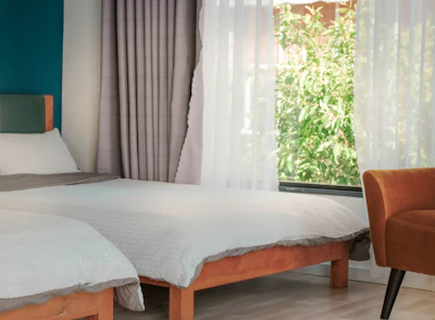 A bright bedroom with large windows, light curtains, and a neatly made bed.