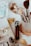 A variety of makeup brushes are neatly arranged in a holder, accompanied by several cosmetics items including a lipstick and perfume. The setting has an elegant yet casual feel, with soft lighting highlighting the textures and colors of the beauty products.