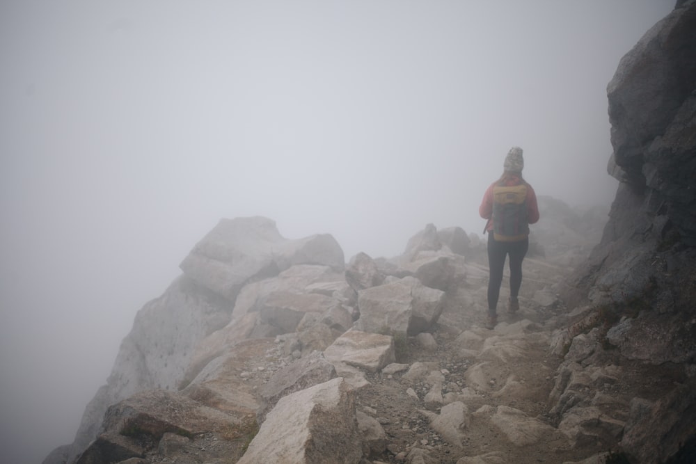 uma pessoa caminhando até uma montanha rochosa em um dia de nevoeiro