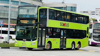A bright green double-decker bus is prominently displayed with 'SG❤️BUS' and route number 67 on the front. The destination is set for Choa Chu Kang via Bt Timah Rd. The background shows an urban setting with additional buses and modern buildings.