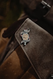 A close-up of a fabric bag adorned with an enamel pin. The pin features a cute character with a smiling face and the words 'Felix Felicis' above and below it in a ribbon banner. The bag material appears textured and is likely made from canvas.