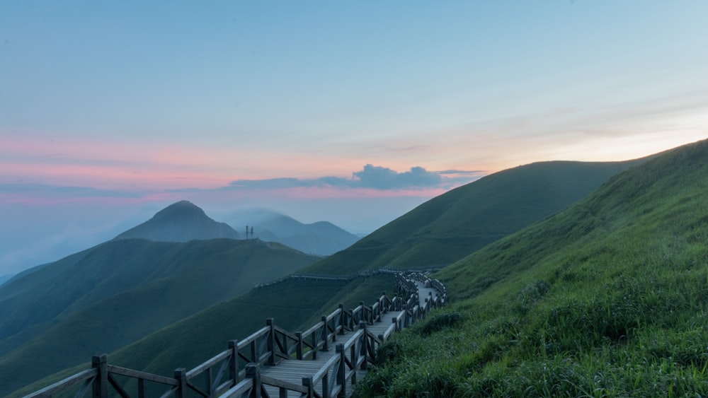 a wooden walkway on a grassy hill with mountains in the background