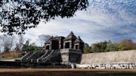 Ancient temple ruins framed by vibrant tropical flowers under a bright blue sky.