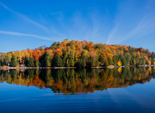 A serene lake reflecting colorful fall foliage and distant hills.